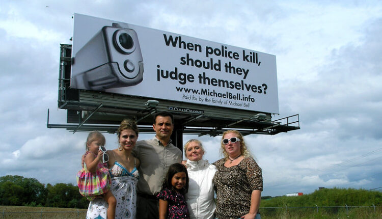 Michael Bell Sr. (center) and his family stand in front of one of the many billboards they bought to draw attention to internal police investigations after his son was fatally shot by Kenosha police in 2004. (Photo via Bell