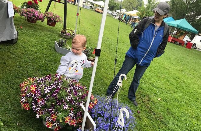 Penelope Britton, left, and mom Meghan stop to smell the flowers May 28 at the Cazenovia Farmers Market.  The market is from 9 am to 2 pm Saturdays on Green Street.