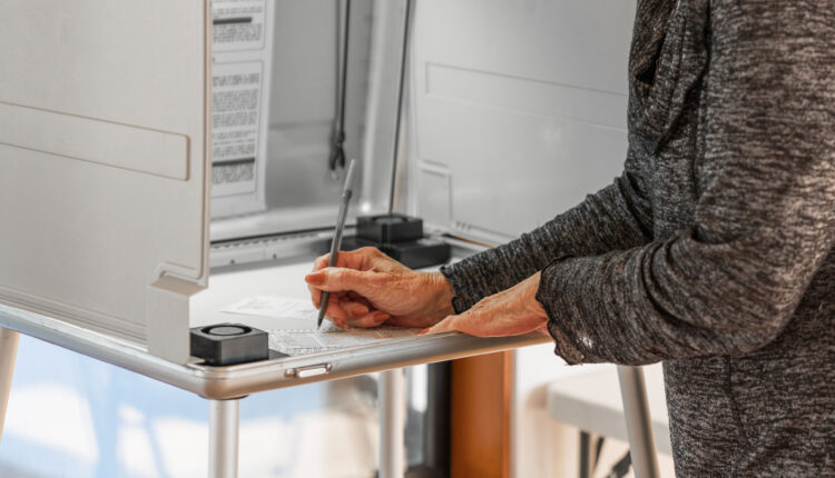 A woman standing at a voting booth marks a ballot.