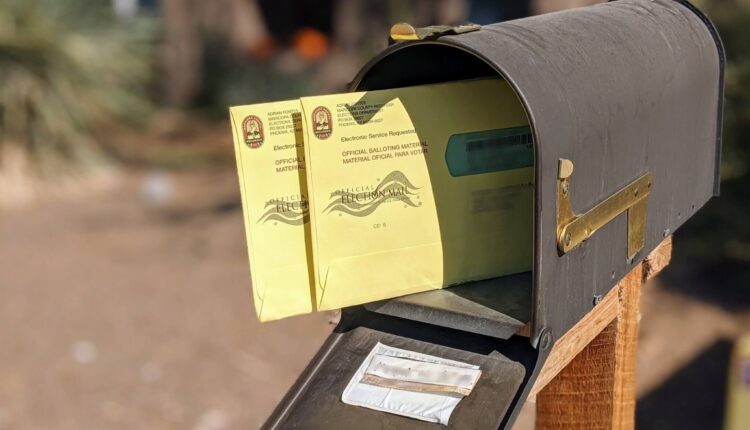 Two absentee ballots in the mail sticking out of the front of a mail box on a pole