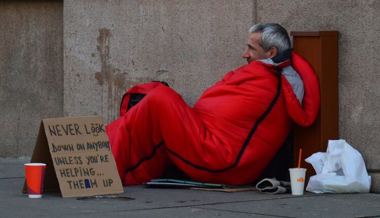 Homeless man & advice on sign in red sleeping bag on the street