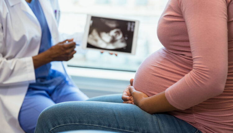 A photo of a black doctor showing a black pregnant woman an image of her ultrasound.