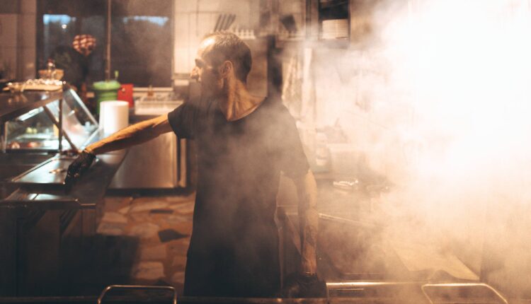 A photo of a man working in a steamy restaurant kitchen.